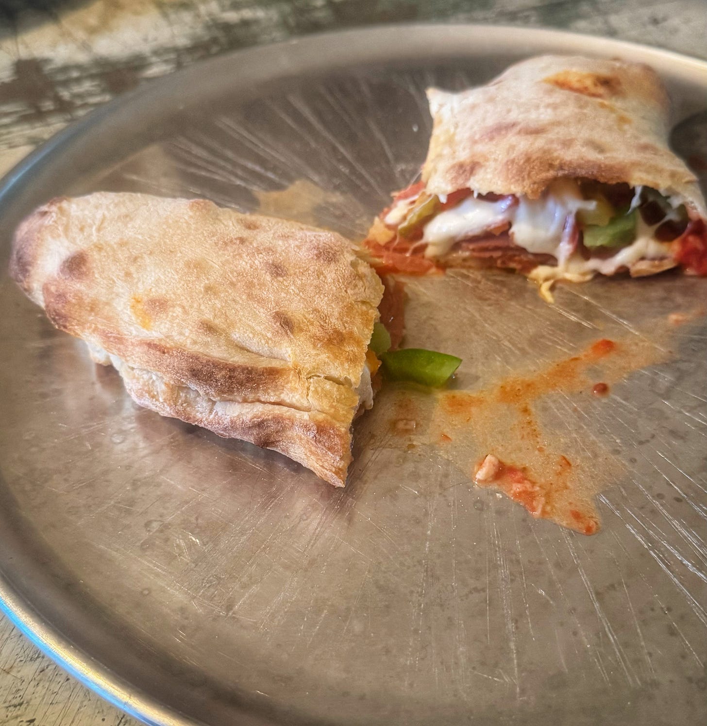 The cut-open calzone on a pizza tray. There is tomato sauce, cheese, pepperoni, and green pepper visible inside.