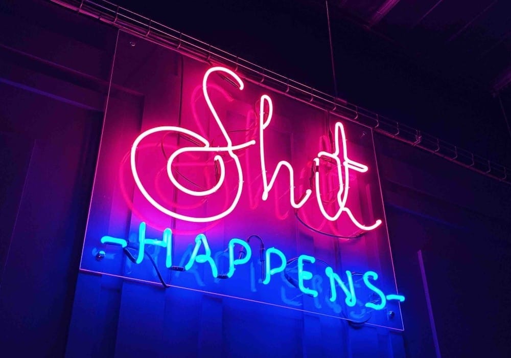 Neon pink and blue sign saying "Shit Happens"