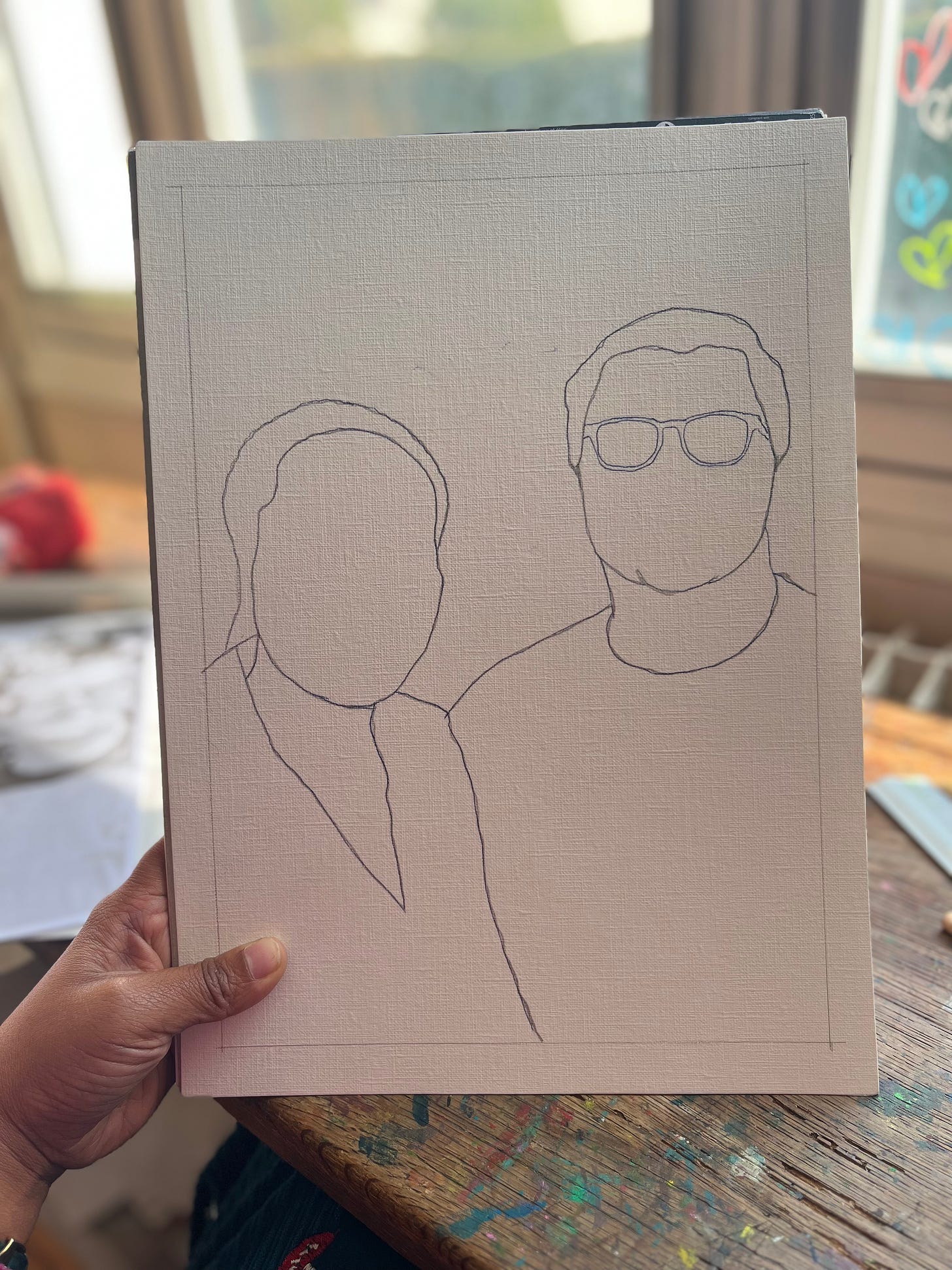 A black hand holding a drawing of a couple's faceless portrait