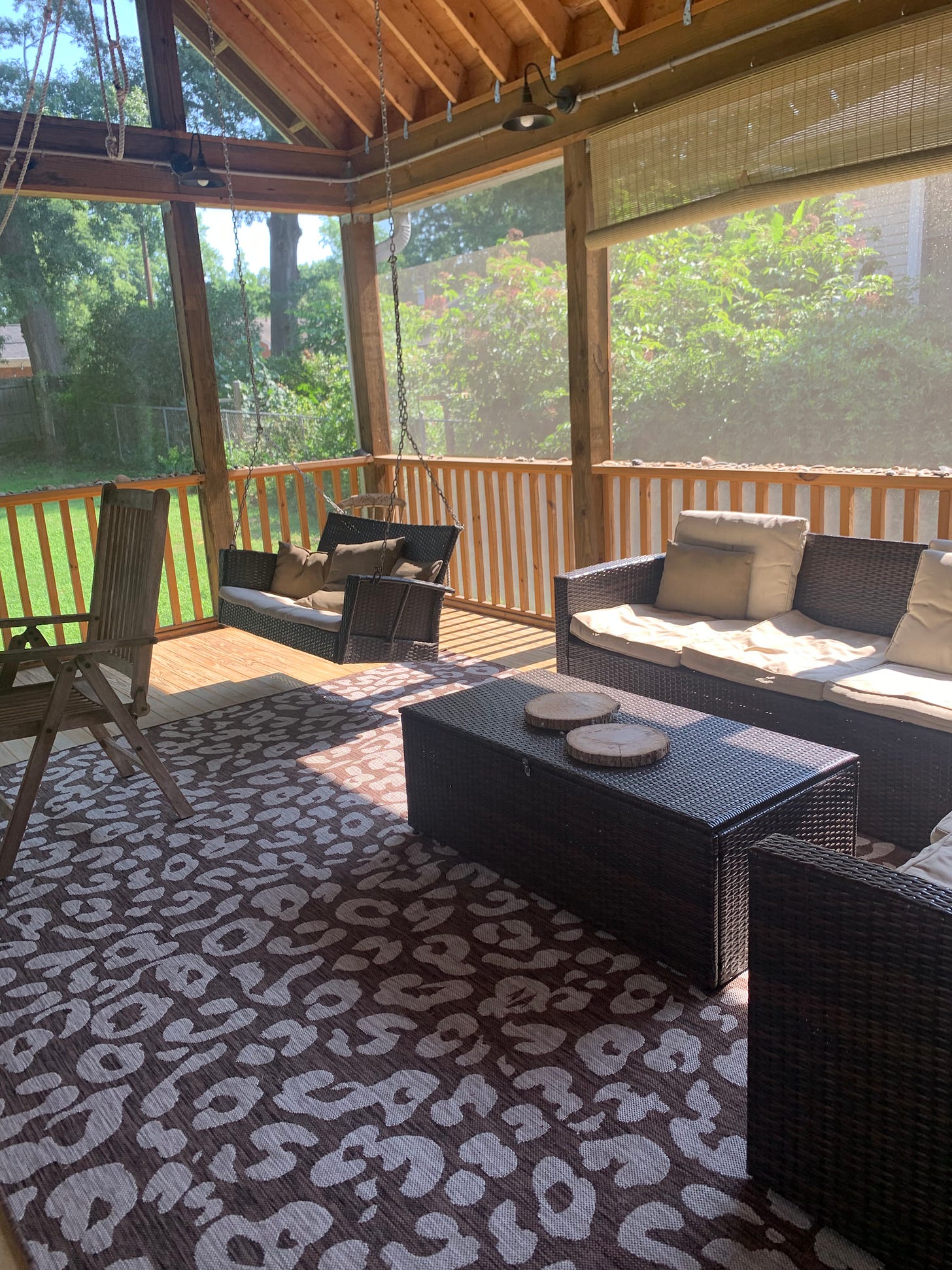 a photo of my enclosed back porch with sofa, swing, rug and dark wood outdoor furniture, all very sunny