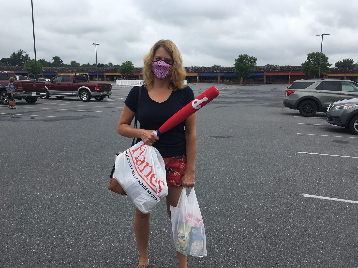 Woman standing in an outlet mall parking lot with bags and a Phillies bat in hand