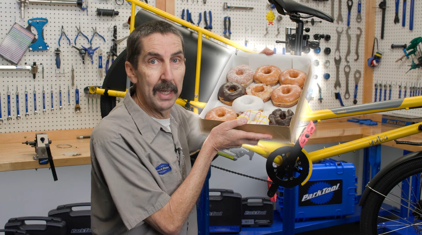 Un mecanicien montrant une grosse boite de donut devant un atelier de reparation