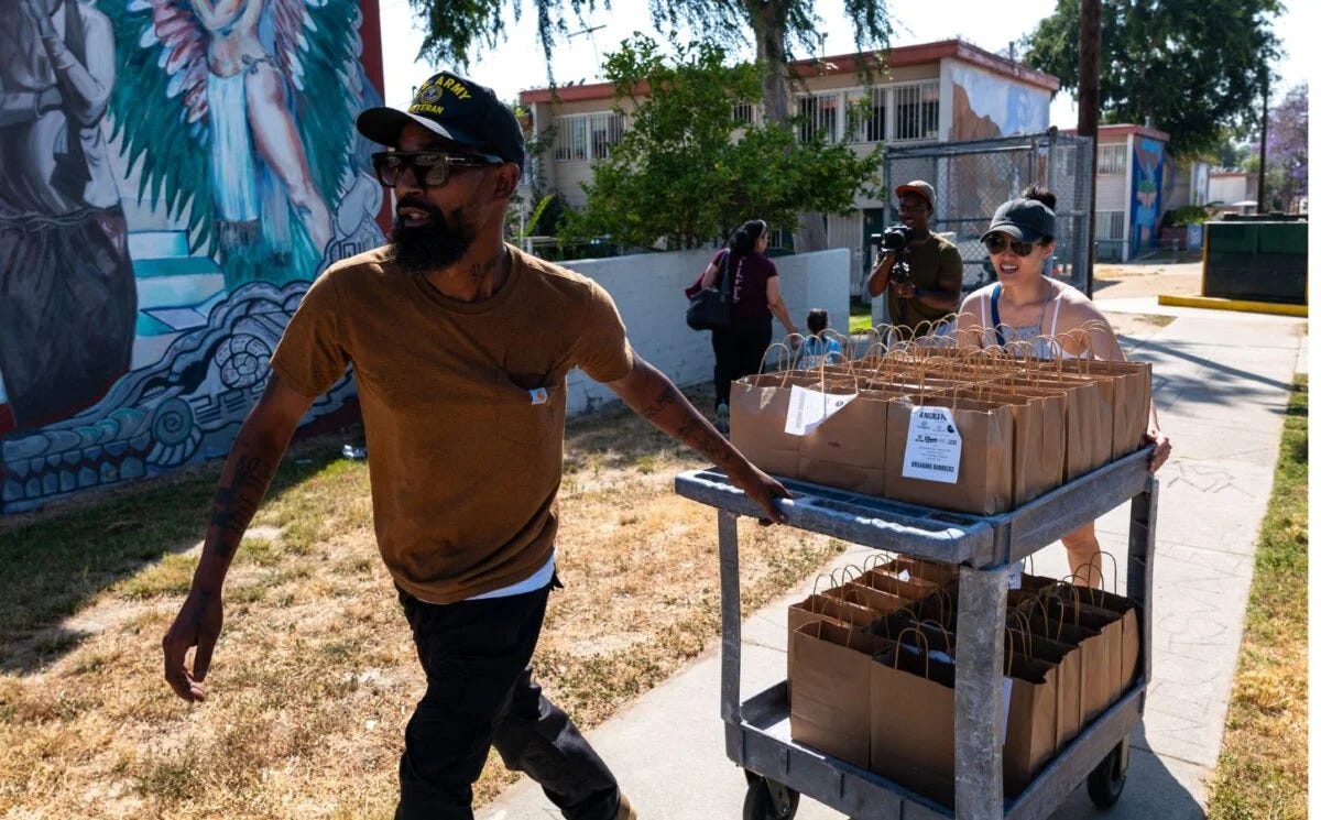 Chef helping someone drag a cart full of Vegan food across a sidewalk.