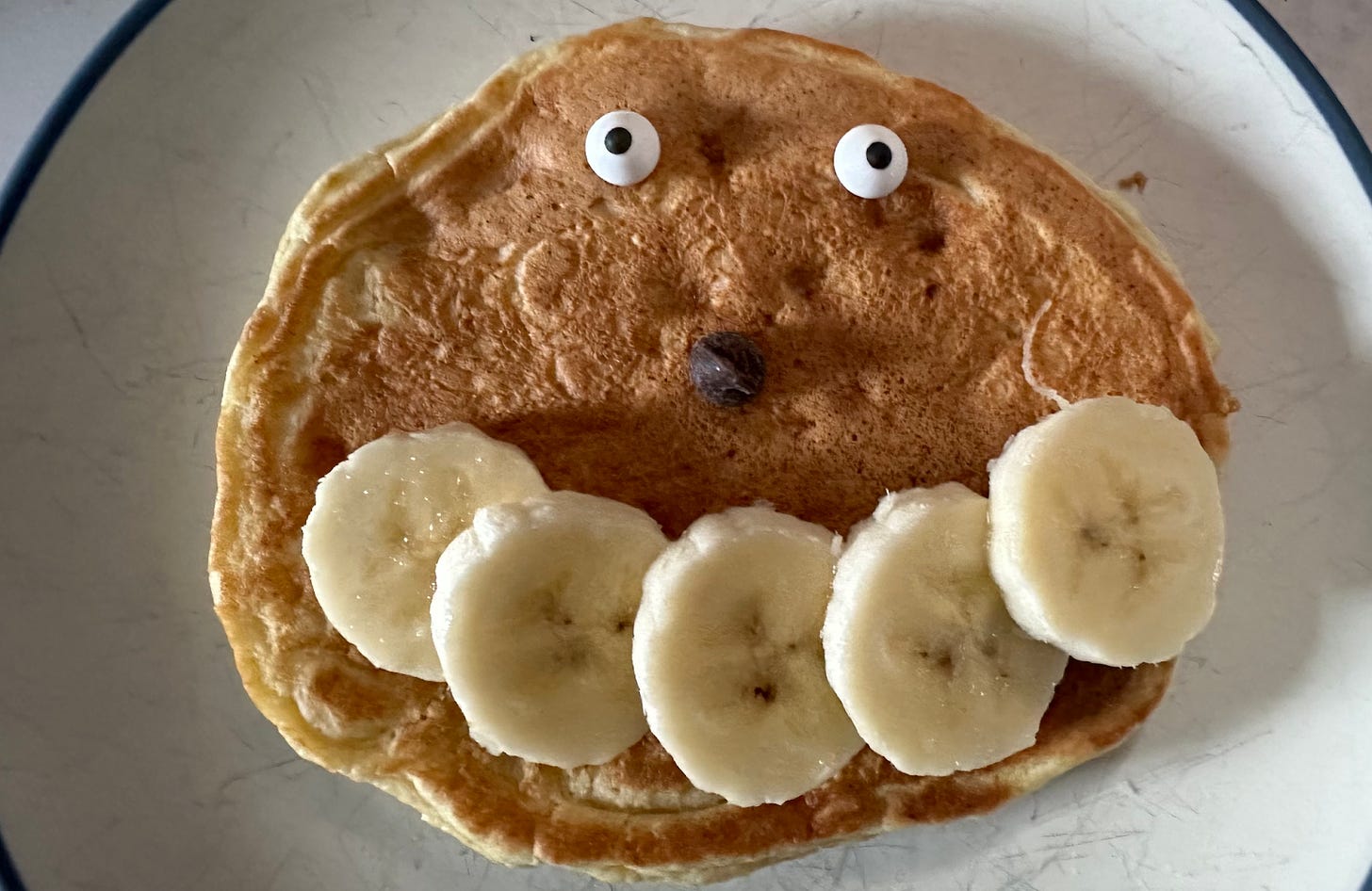 Pancake with googly eyes, a chocolate chip nose, and bananas for a smile