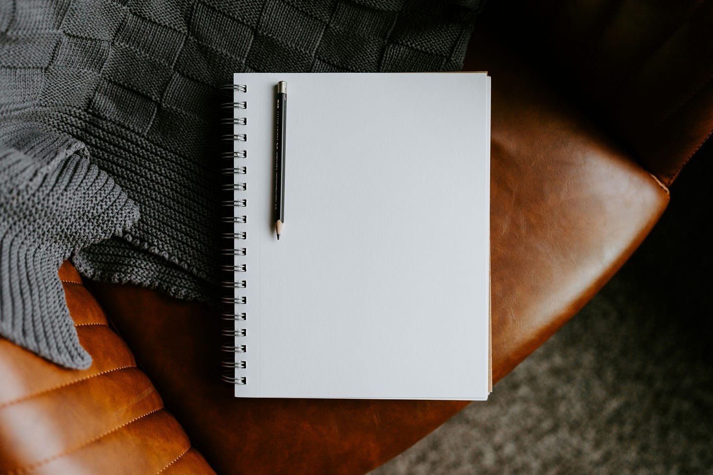 blank notebook and pencil on leather couch with blanket