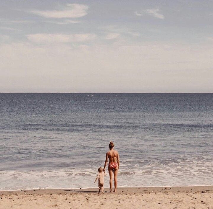 This may contain: a woman and child are walking on the beach