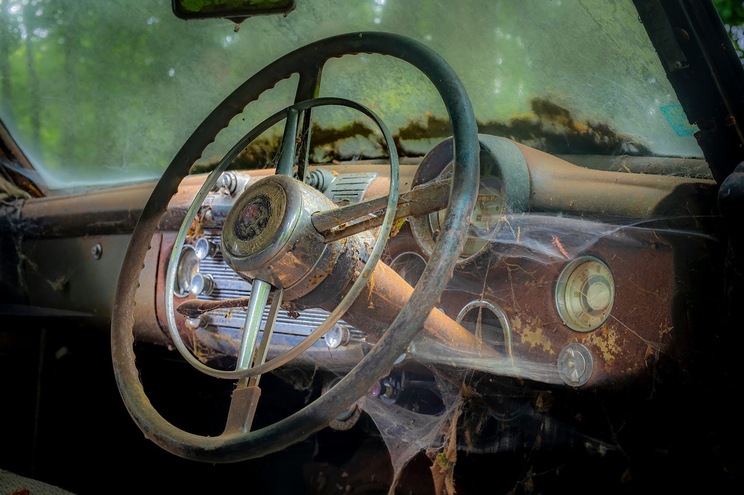 The rusted and cobweb covered steering wheel and dashboard of an abandoned car.