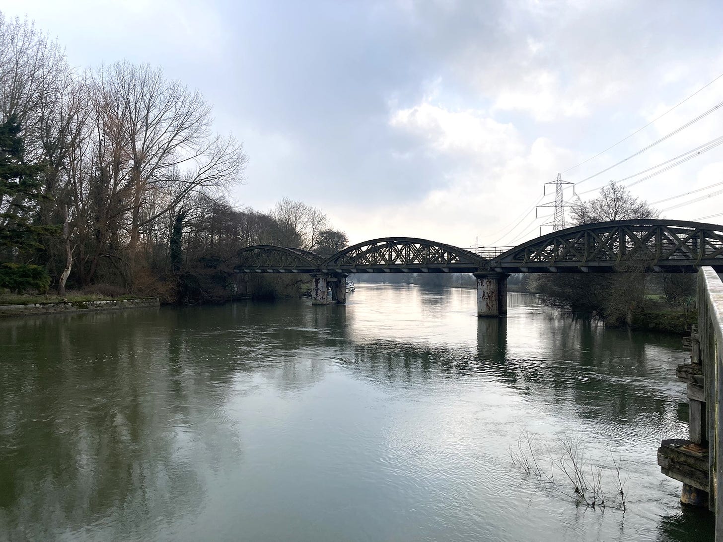 Old rail bridge over the River Isis. It's a blue-grey day, which is reflected in the water.