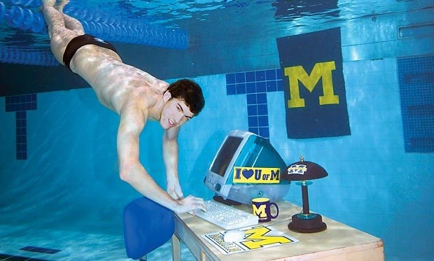 Michael Phelps swimming beneath the water and typing on an underwater computer desk.