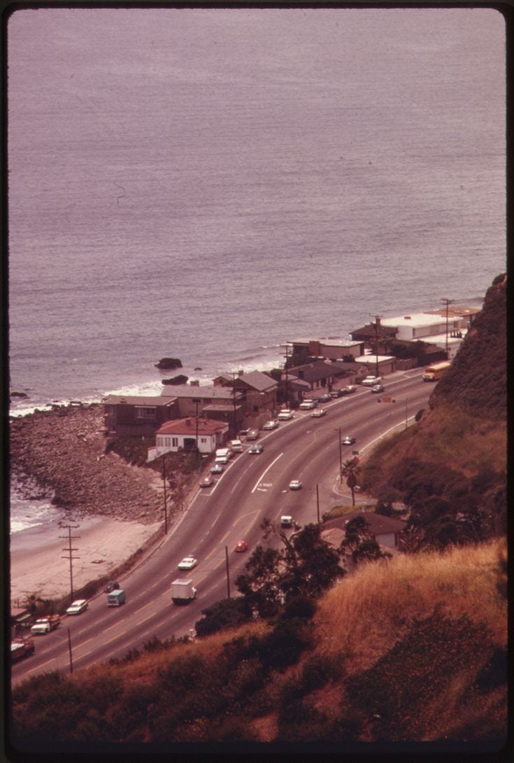 This may contain: an aerial view of the ocean with cars driving on it's road and beach in the background