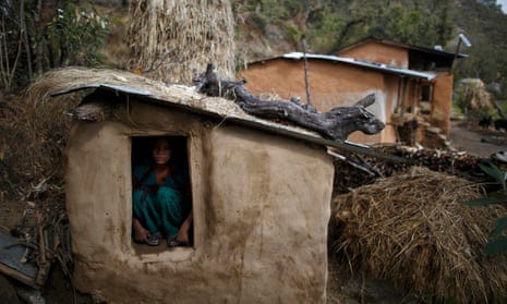 Girl looks through open door of mud-built shelter walled off from homes in background