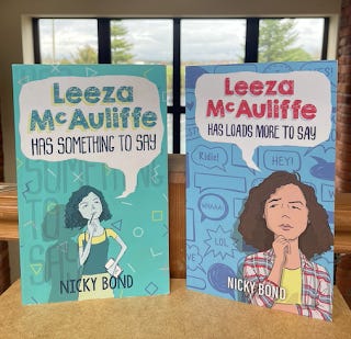 Two books, side by side, propped up on a desk with a window in the background. The book on the left is called Leeza McAuliffe Has Something To Say. The book on the right is called Leeza McAuliffe Has Loads More To Say. Both books are by me, Nicky Bond.