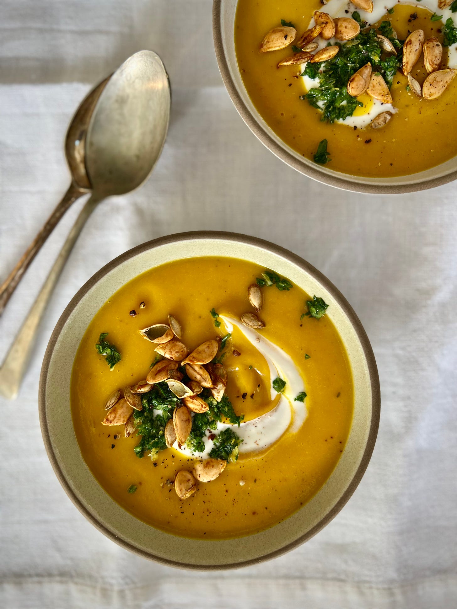 two bowls of pumpkin soup with spicy pumpkin seeds and gremolata topping