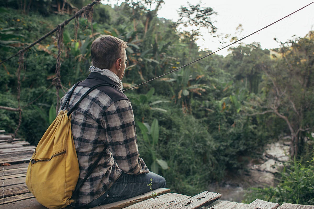 "Young Man With Backpack Sitting And Thinking On A Wooden Bridge Overlooking The Jungle" by ...