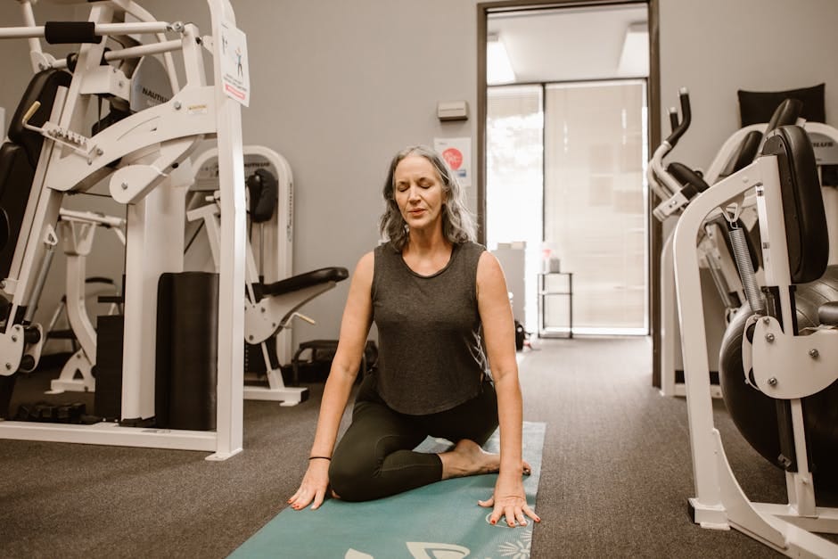 A midlife woman meditates on a yoga mat in a gym, practicing mindfulness and wellness.