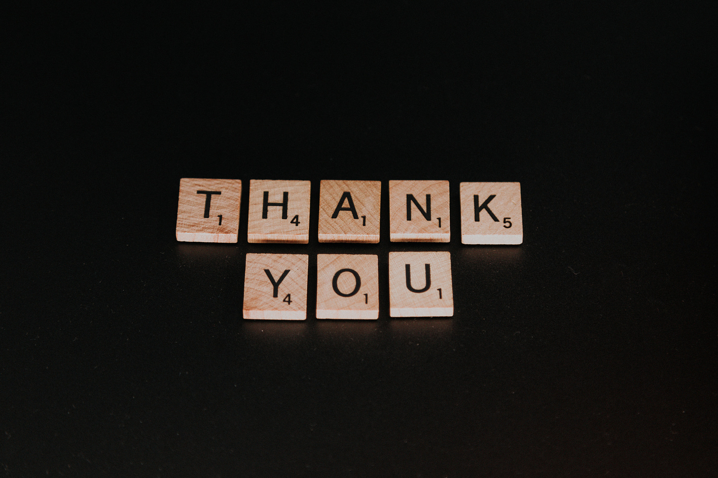 Scrabble tiles spelling out "Thank you" set against a black background. Thank is on the top row, you on the bottom.