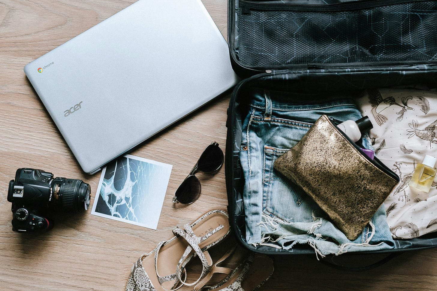 Wood surface with an open suitcase that’s being packed. To the left, there’s an SLR camera and laptop.