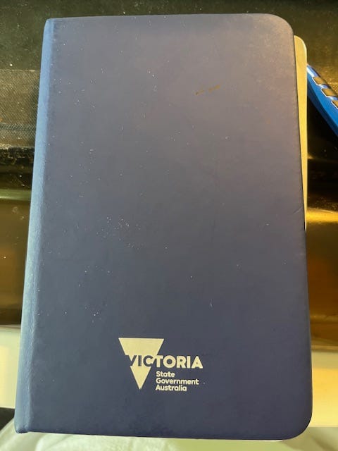 A closed blue notebook with the words "Victoria: State Government Australia" in white letters.