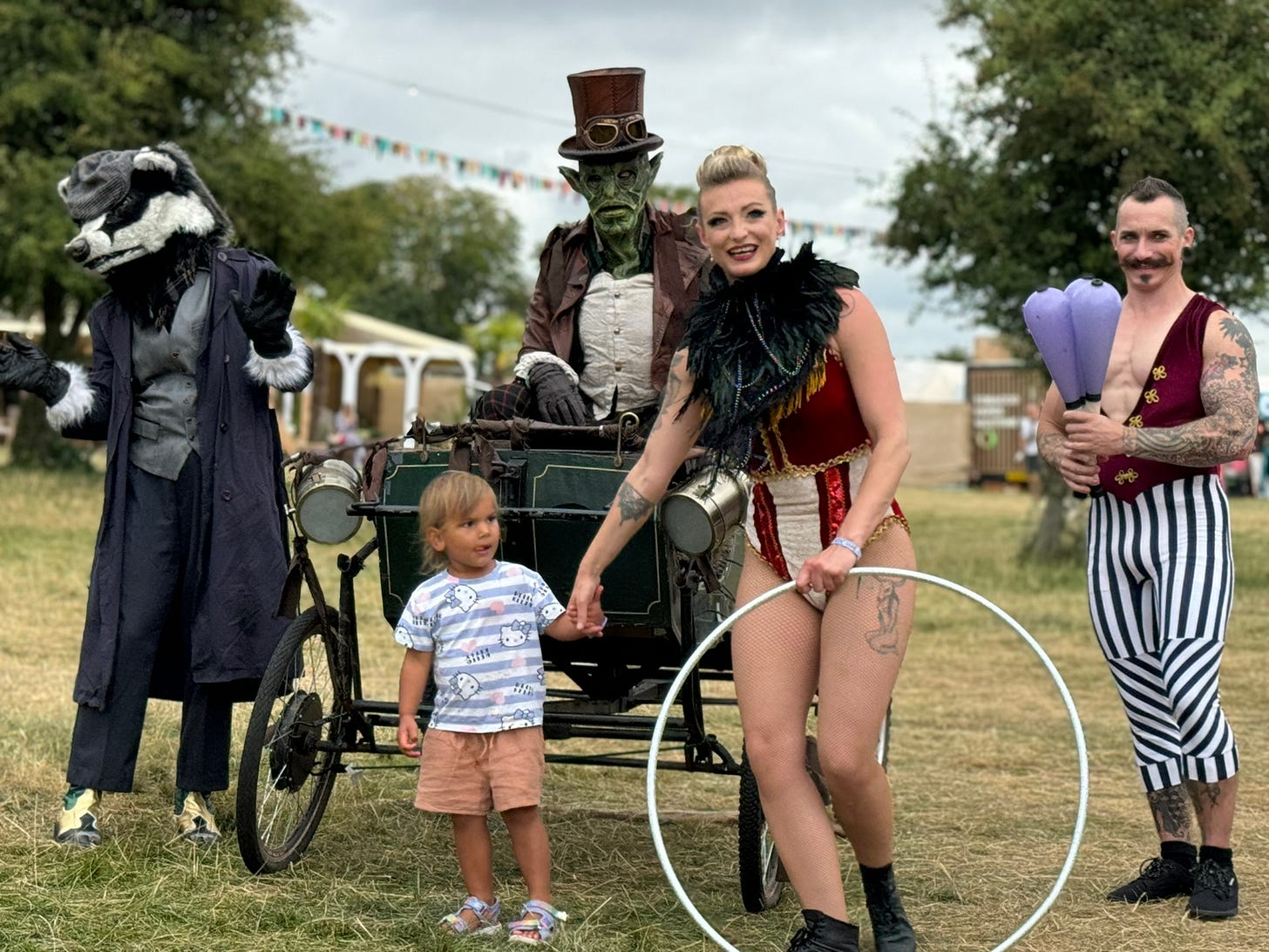 Entertainers are dressed as a badger, a scary looking toad who is in a carriage, A circus juggler and an acrobat lady.  She is holding a small childs hand.  