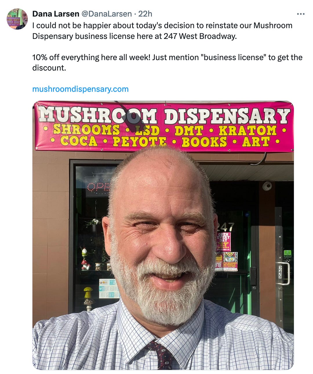 Post on X from @DanaLarsen that reads: "I could not be happier about today's decision to reinstate our Mushroom Dispensary business license here at 247 West Broadway.  10% off everything here all week! Just mention "business license" to get the discount." It also includes a photograph of Larsen, a smiling white man with a grey beard wearing a dress shirt and tie, standing in front of a store sign that reads: Mushroom Dispensary - Shrooms, LSD, DMT, Kratom, Coca, Peyote, books, art.