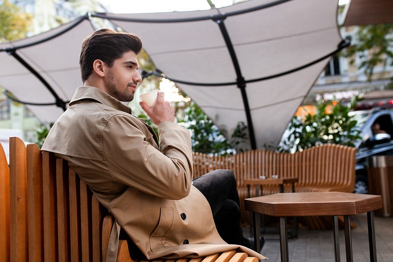 Man wearing a trench coat in an outdoor cafe
