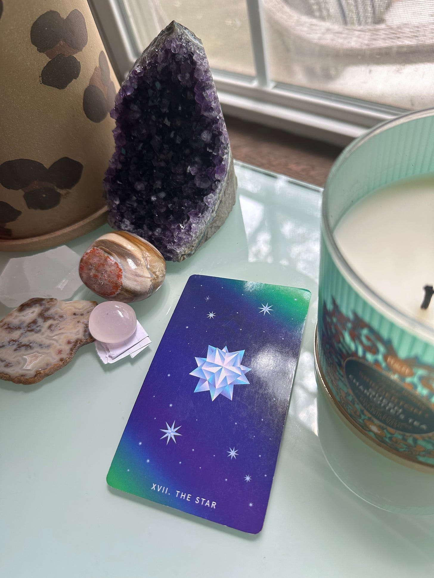 The Star Tarot card sits on a table between crystals and a candle.