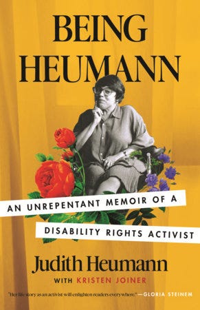 Book cover of Being Heumann: An Unrepentant Memoir of a Disability Rights Activist by Judith Heumann and Kristen Joiner. The background is a yellow-orange color and in the center is a black and white image of Judith, a white Jewish disabled woman in a wheelchair. She has dark hair and is wearing glasses. One of her hands is resting under her chin. Around Judith are illustrations of colorful flowers. 
