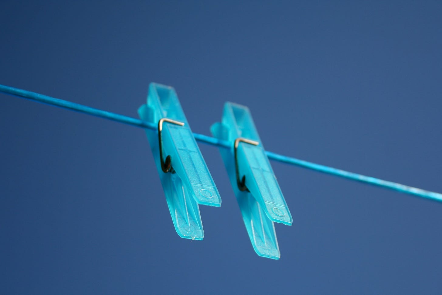 Sfondo blu con un filo azzurro che lo attraversa orizzontalmente, in obliquo verso il basso. Appese al filo ci sono due mollette color azzurrino.