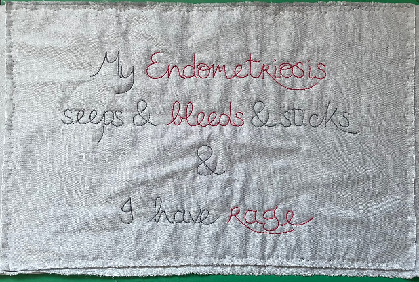 A quilted piece of white fabric with the words My Endometriosis seeps and bleeds and I have rage