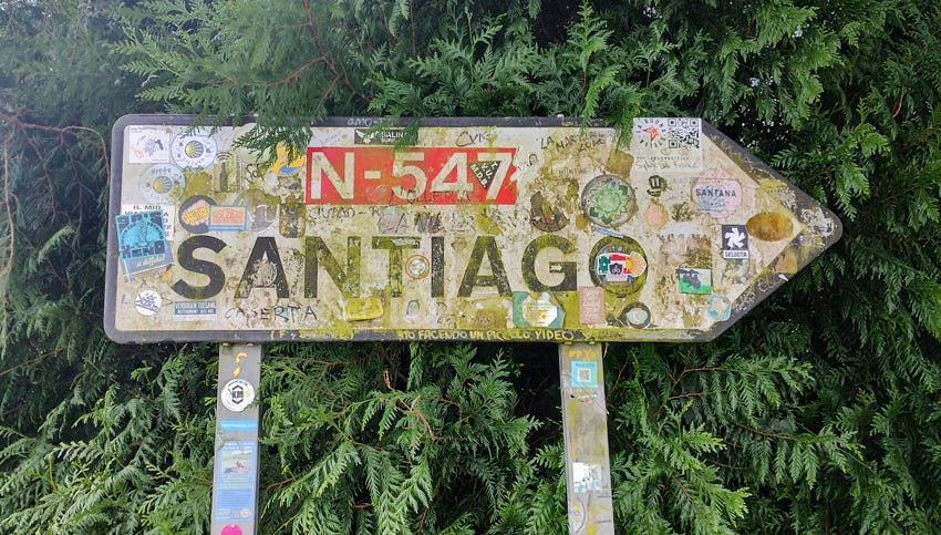 Señal cubierta de pegatinas indicando la dirección a Santiago