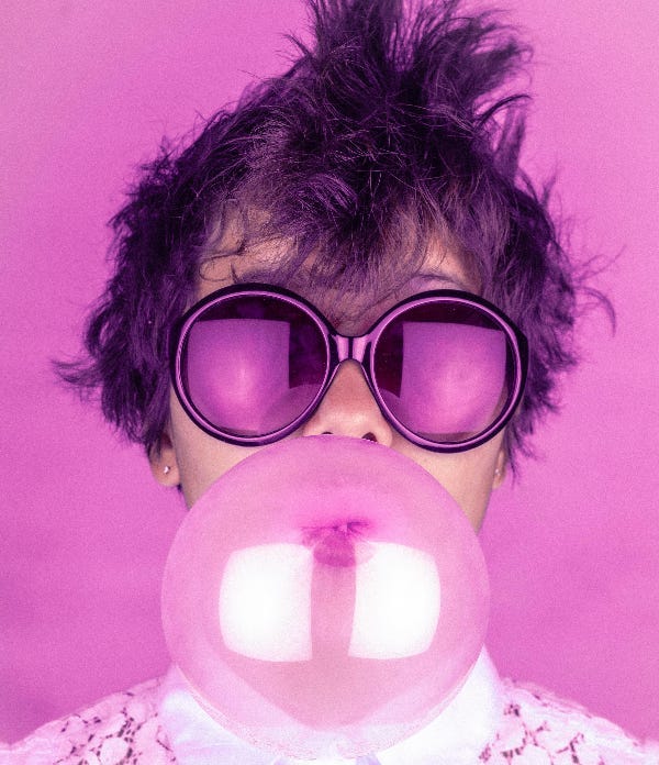 woman in purple sunglasses blowing a big bubble with gum