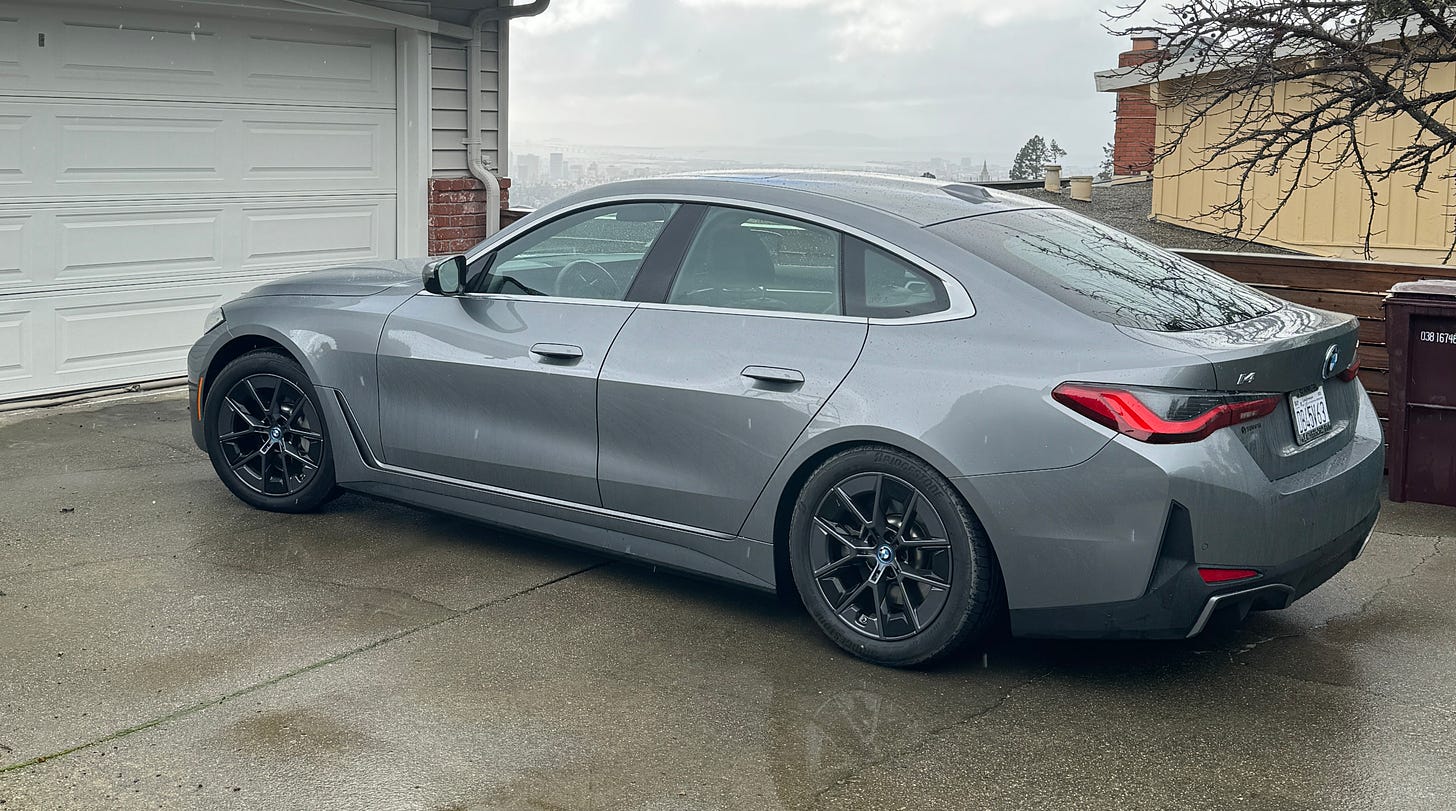 A photo of a silver BMW i4 sitting in a driveway on a rainy day.