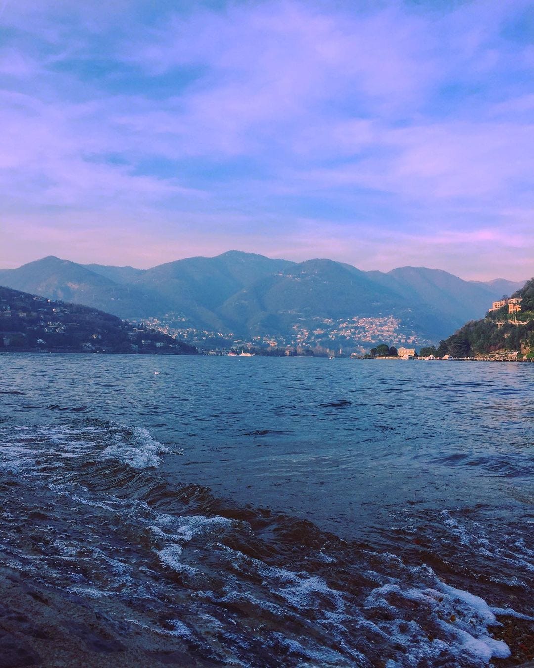 Lake Como is shown with mountains in the background. The image has a slight purple tint.