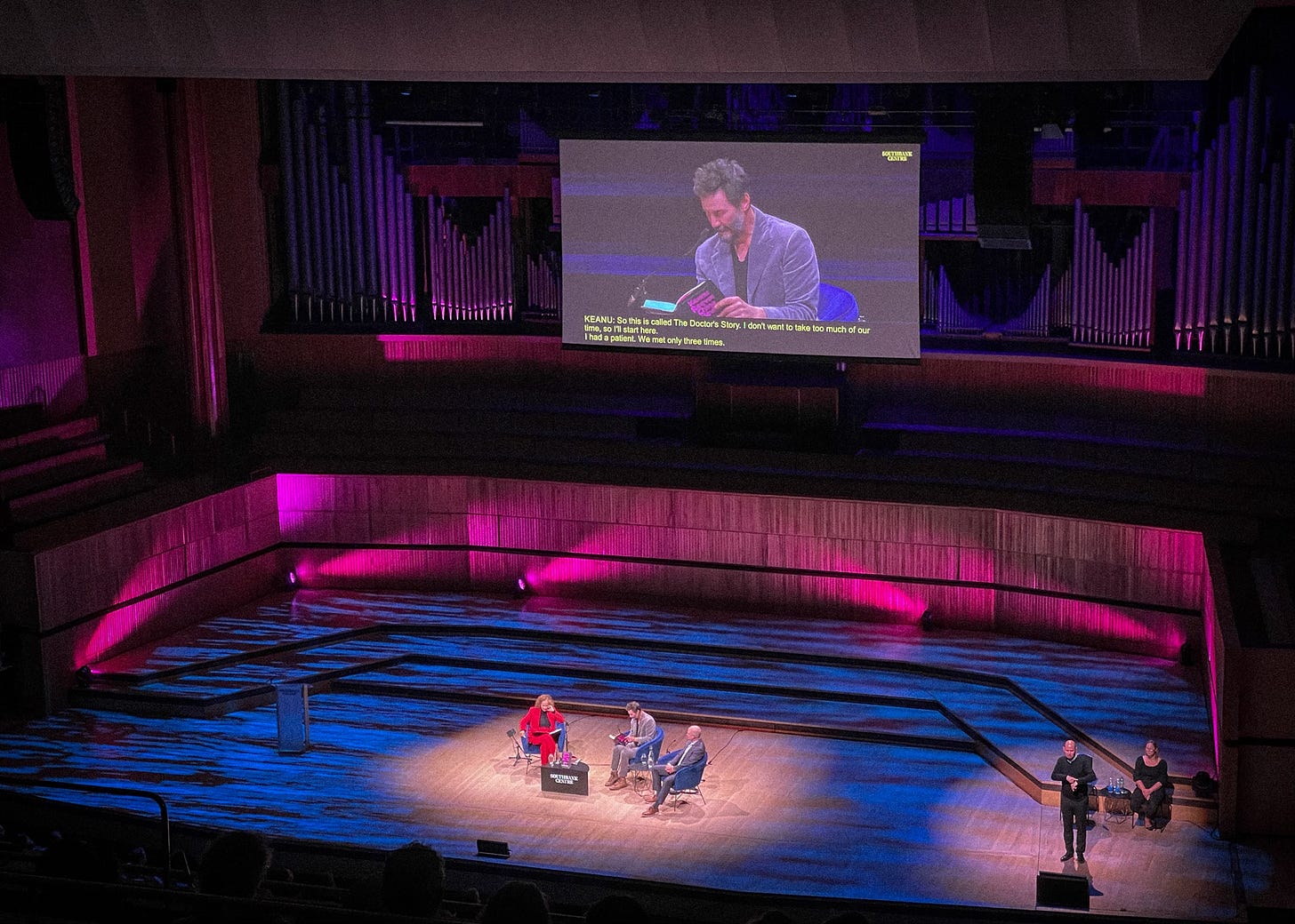 Photograph depicts an auditorium stage. Three guests and two sign language interpreters.