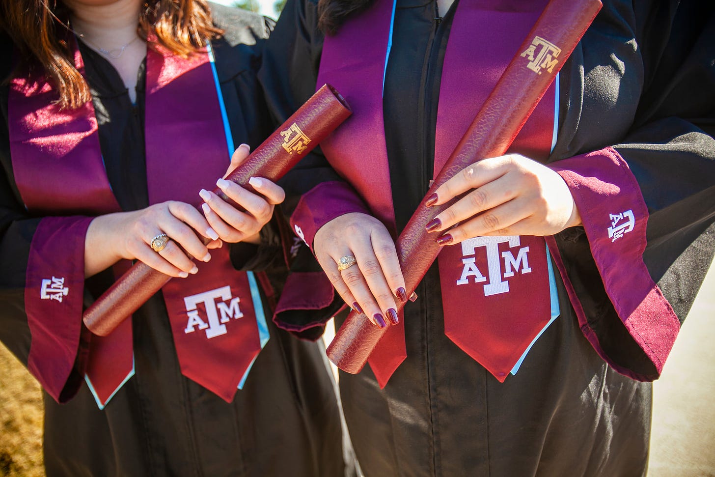 two graduates wearing maroon tamu stoles holding their maroon diploma tubes