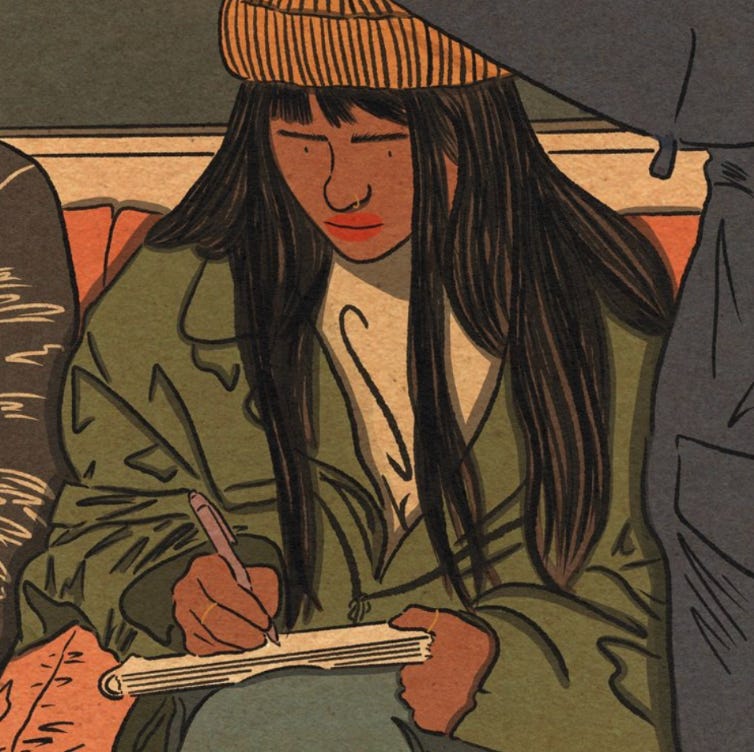 A femme with long black hair and bangs underneath an orange beanie is writing on a notebook while riding the subway