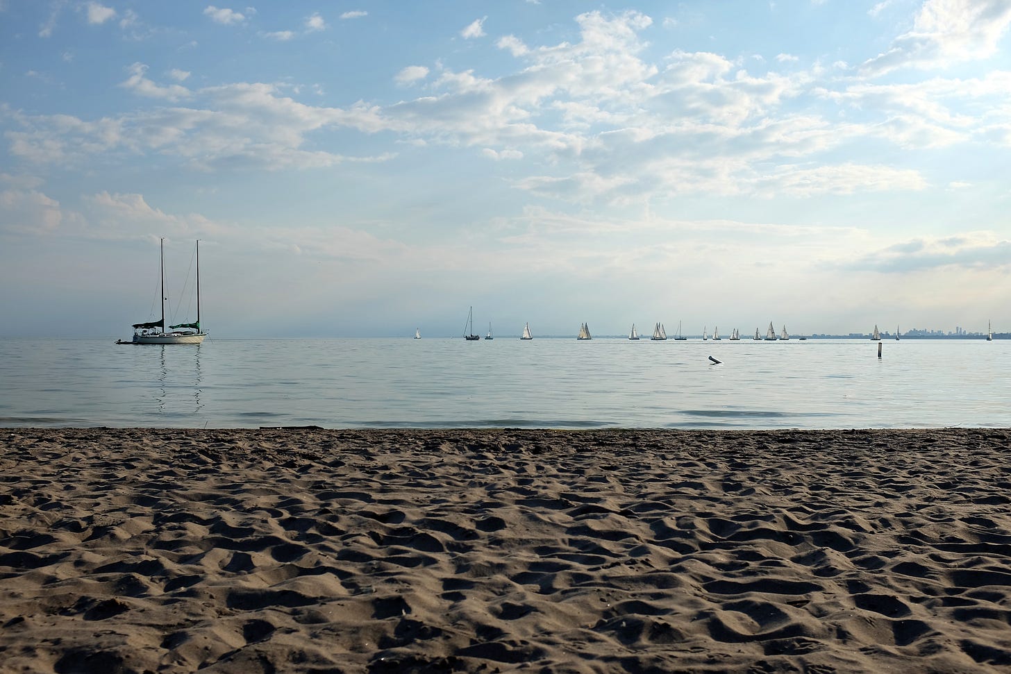 A view of the water at Hanlan's Point Beach with sand in the foreground and several recreational boats in the water just off the coast. A view of the water at Hanlan's Point Beach with sand in the foreground and several recreational boats in the water just off the coast.