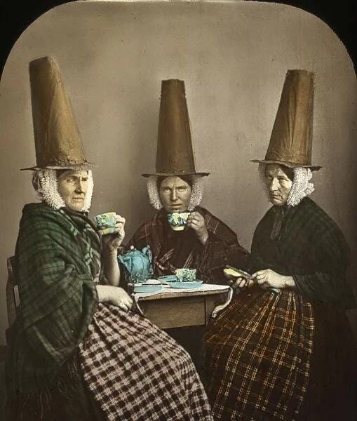 Group of three Welsh women in traditional costume with very tall hats and wearing shawls.