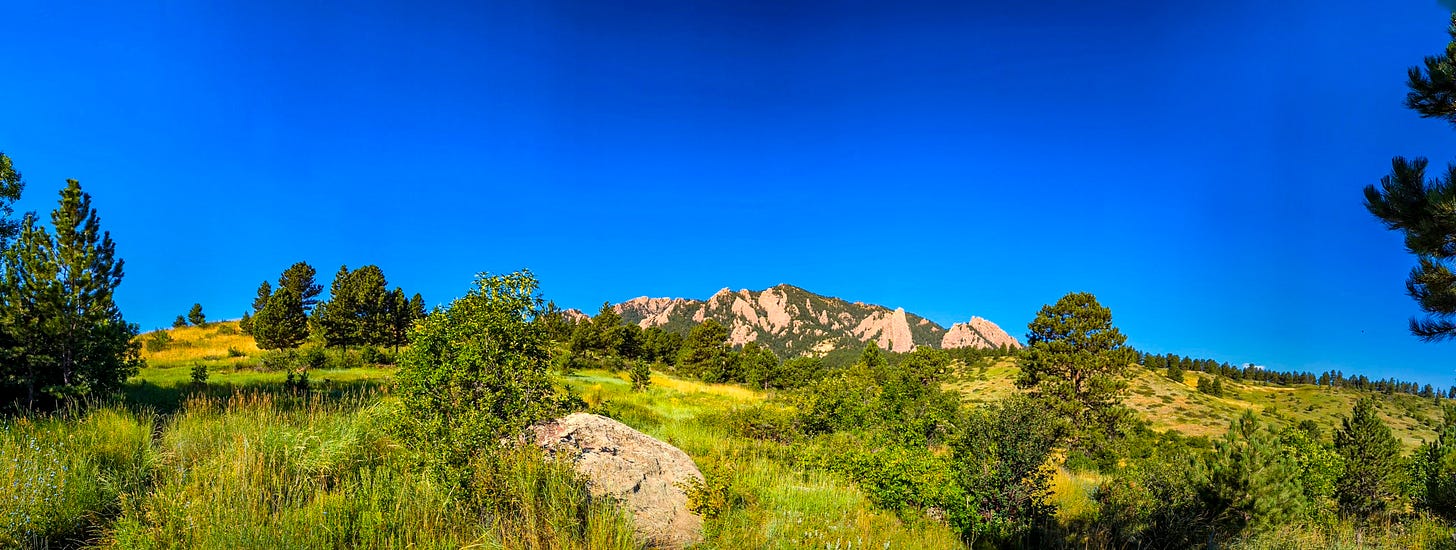 Another view of the Flatirons from a distance, green grass in the foreground. 