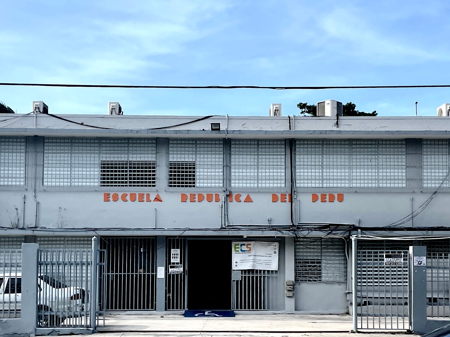 Geometric orange type that says Escuela Republica del Peru on a gray school building in San Juan.