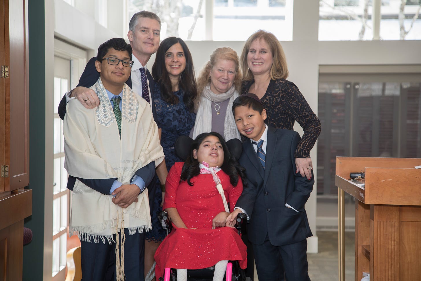 Dalia wears a red dress and sits in a wheelchair surrounded by parents, siblings and Grandma