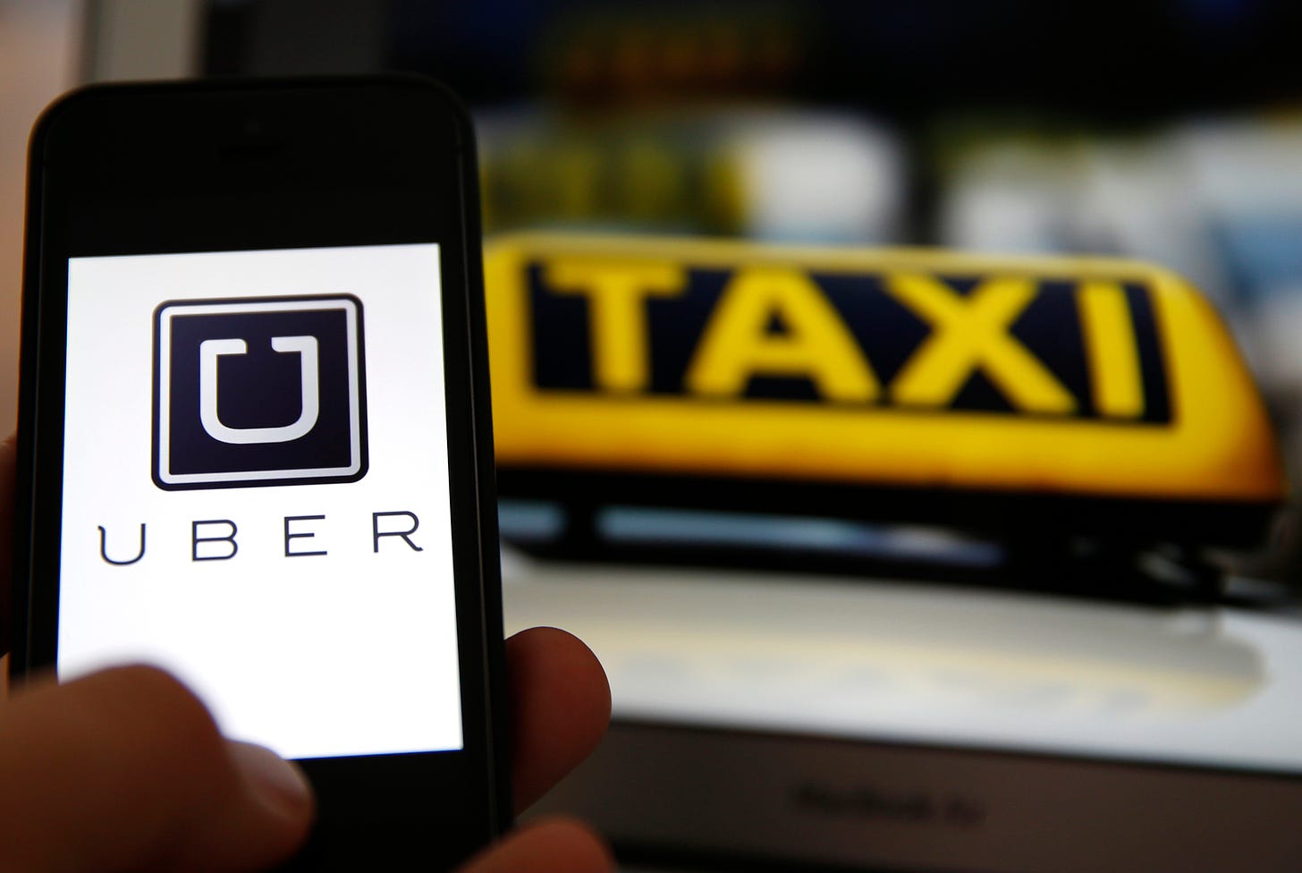 File illustration picture showing the logo of car-sharing service app Uber on a smartphone next to the picture of an official German taxi sign