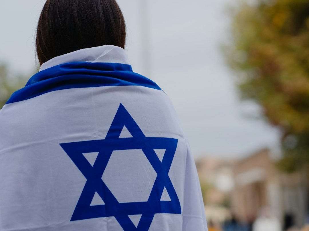woman in white and blue hoodie standing near green trees during daytime