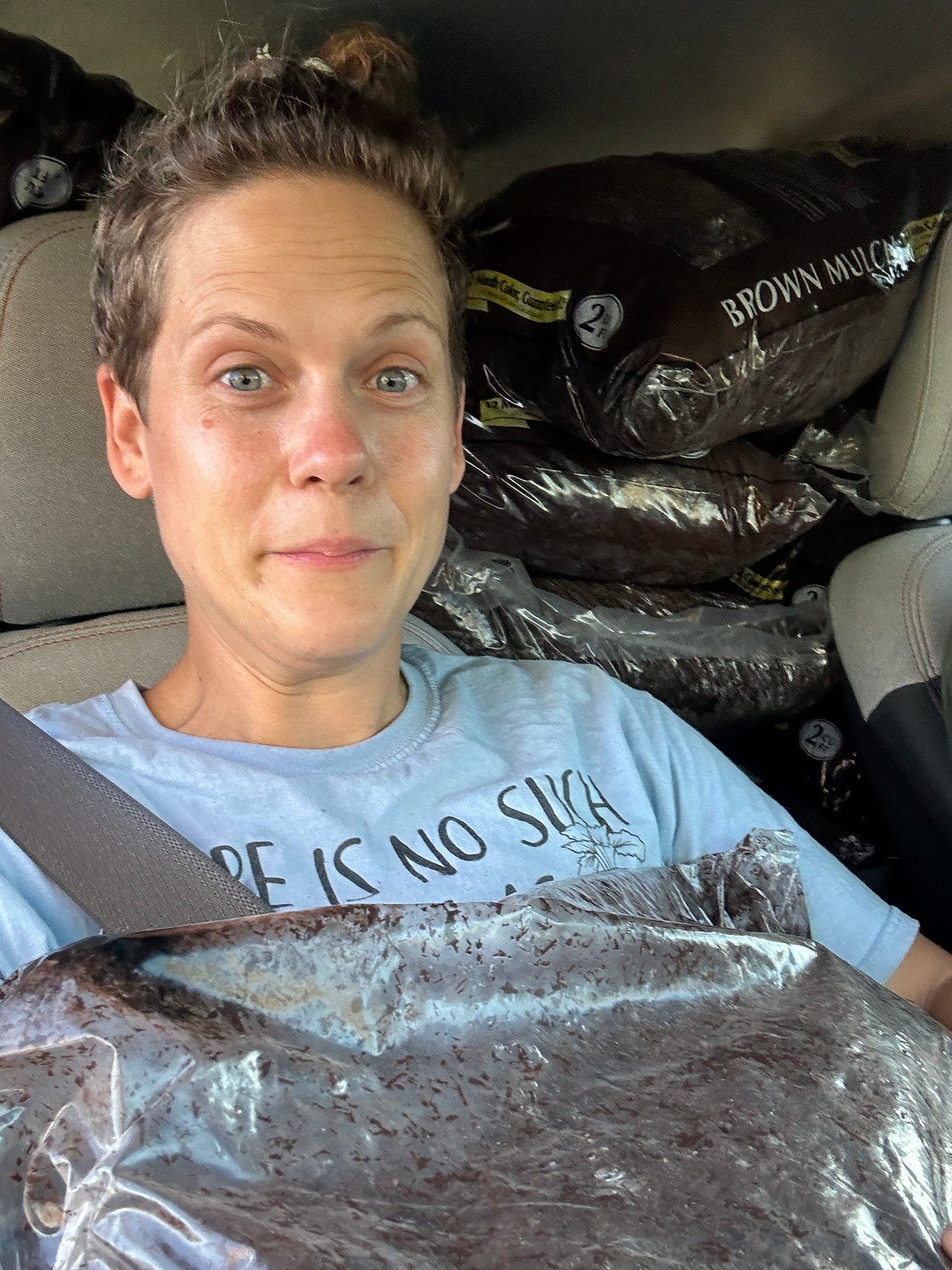  a girl making a silly face in a car packed with mulch behind her and a bag of mulch in her lap