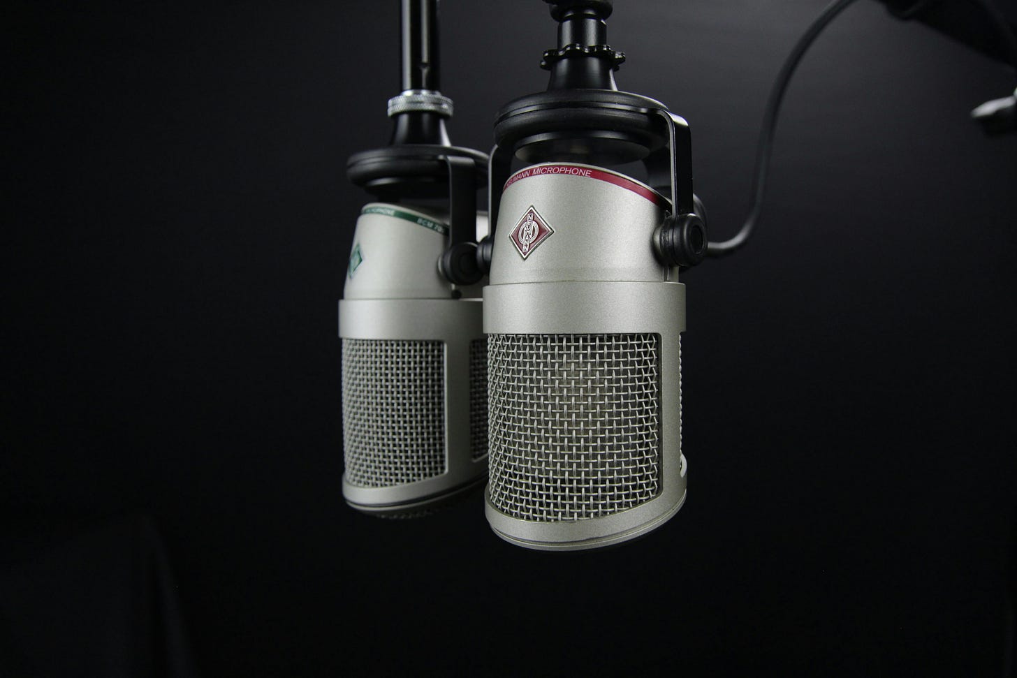 Two silver microphones on a black swing arm stand, in a dark room.