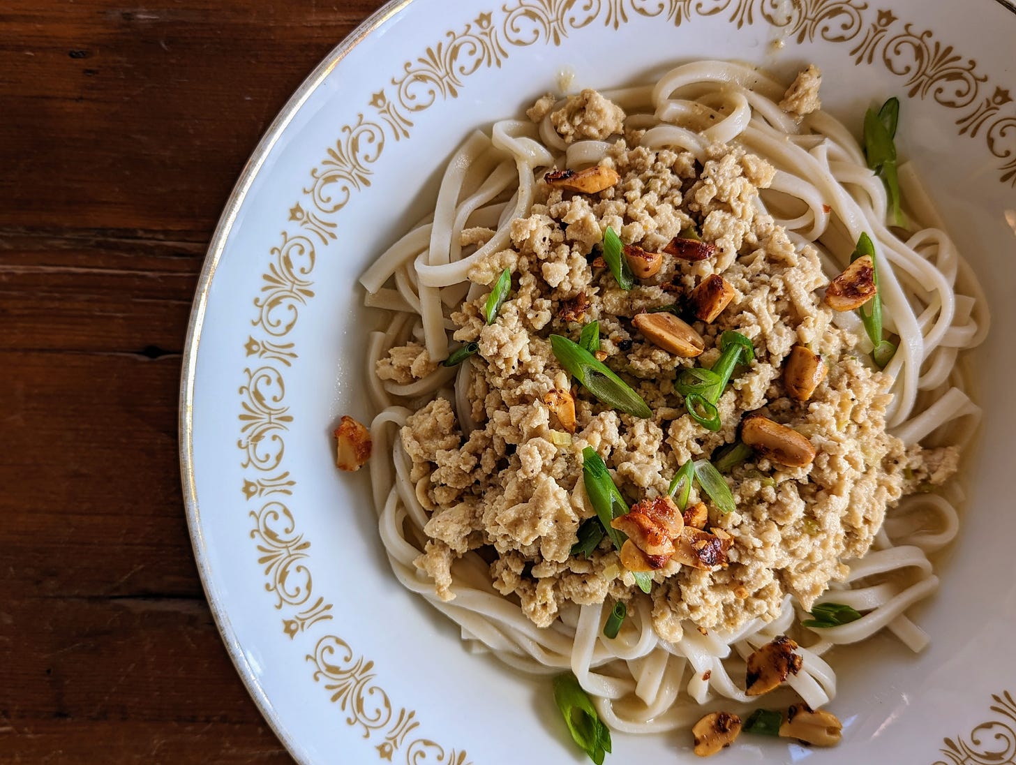 A bowl full of dan dan noodles made with ground chicken and topped with green onions and fried peanuts.