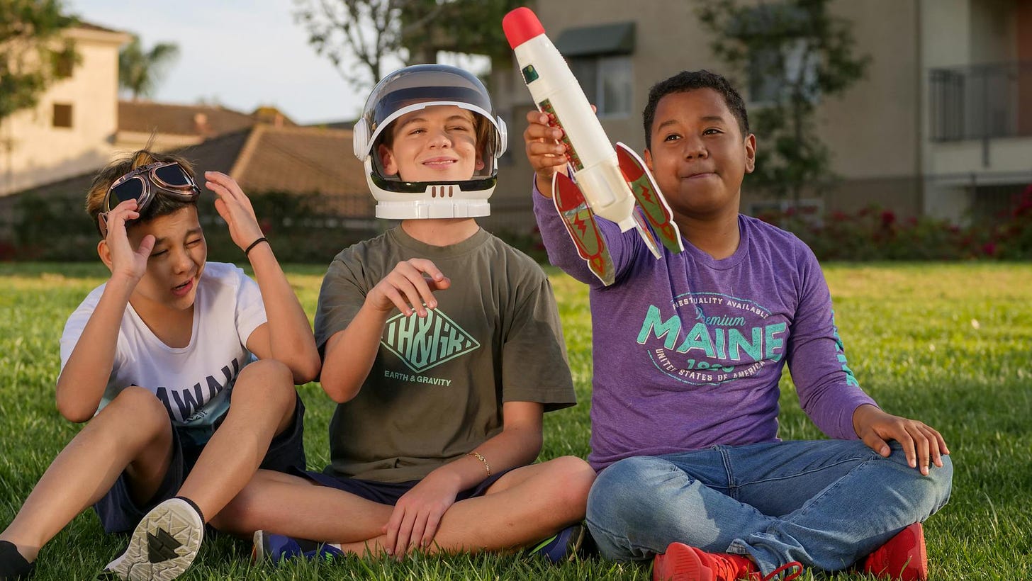 Three boys on a yard playing with a toy rocket