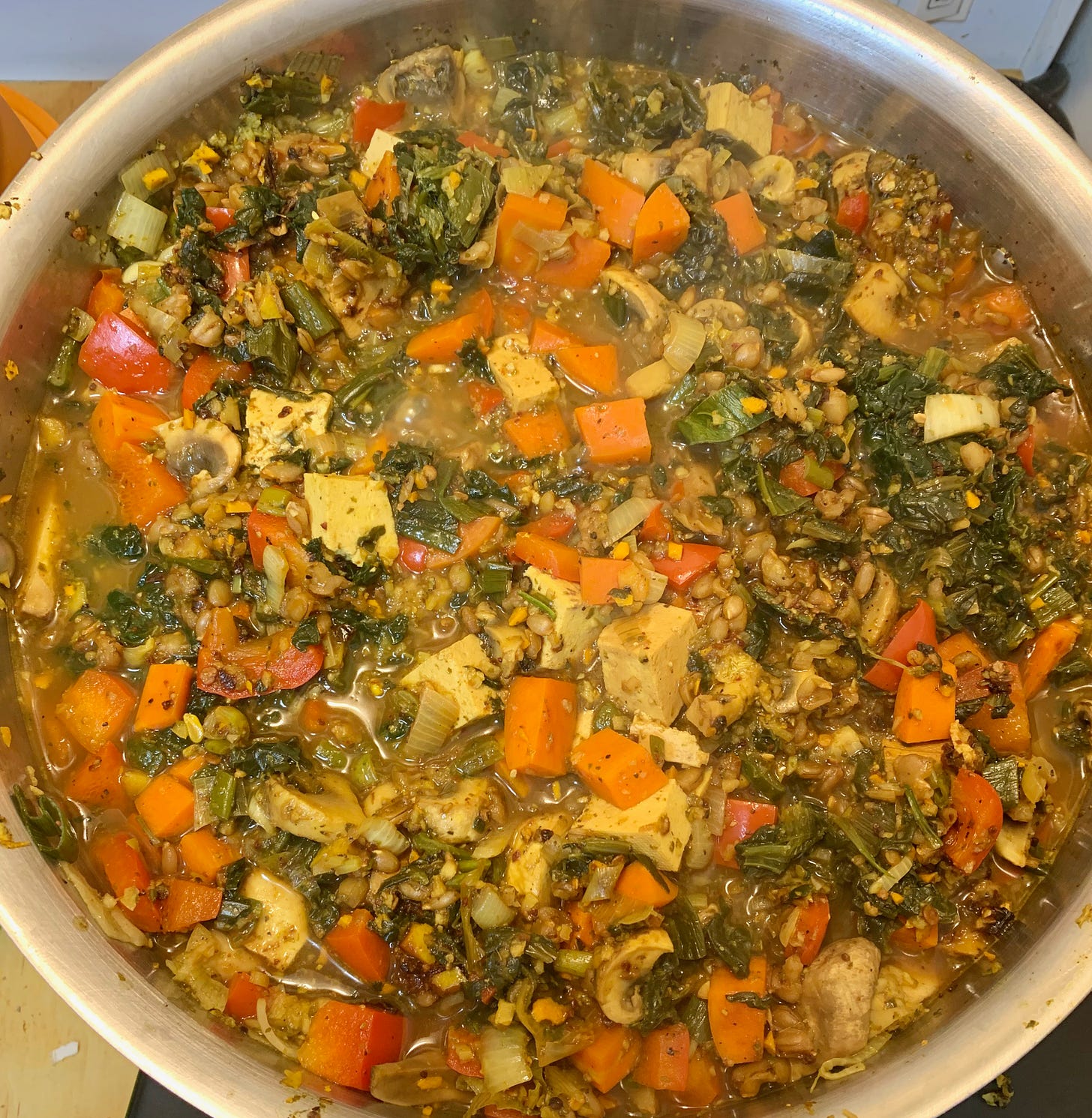A pot of stew in which can be seen spinach, tofu, carrots, mushrooms, and red peppers.