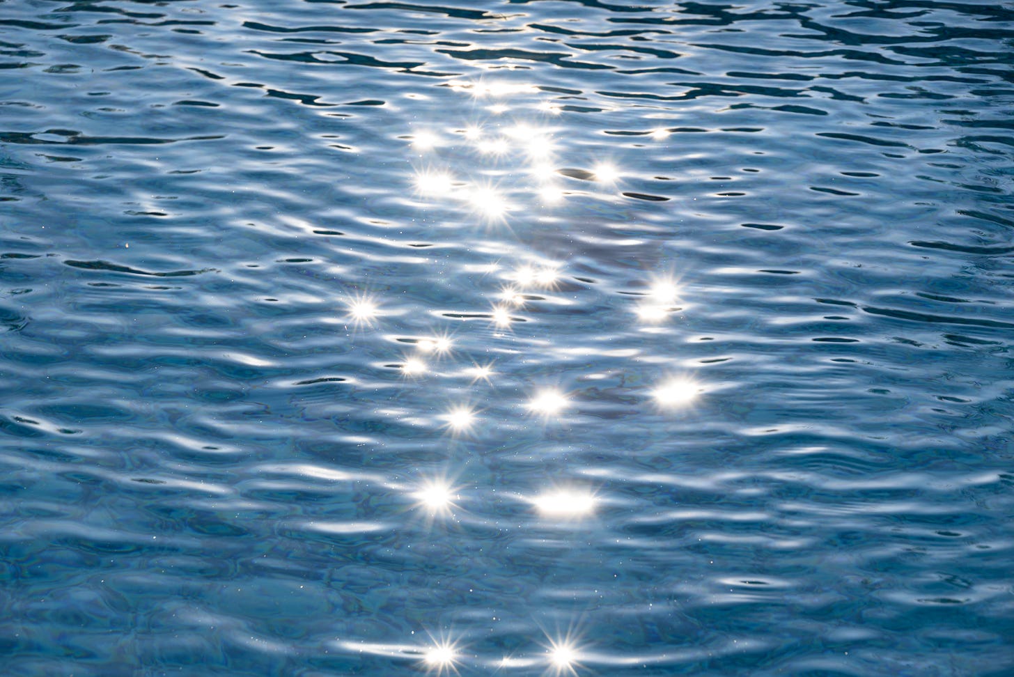 The sun reflects sparkles of light on the surface of a pool of water rippling and blue