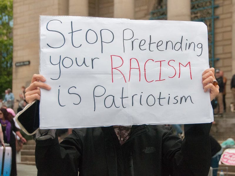 A protester holds up a sign that reads 'Stop pretending your racism is patriotism'